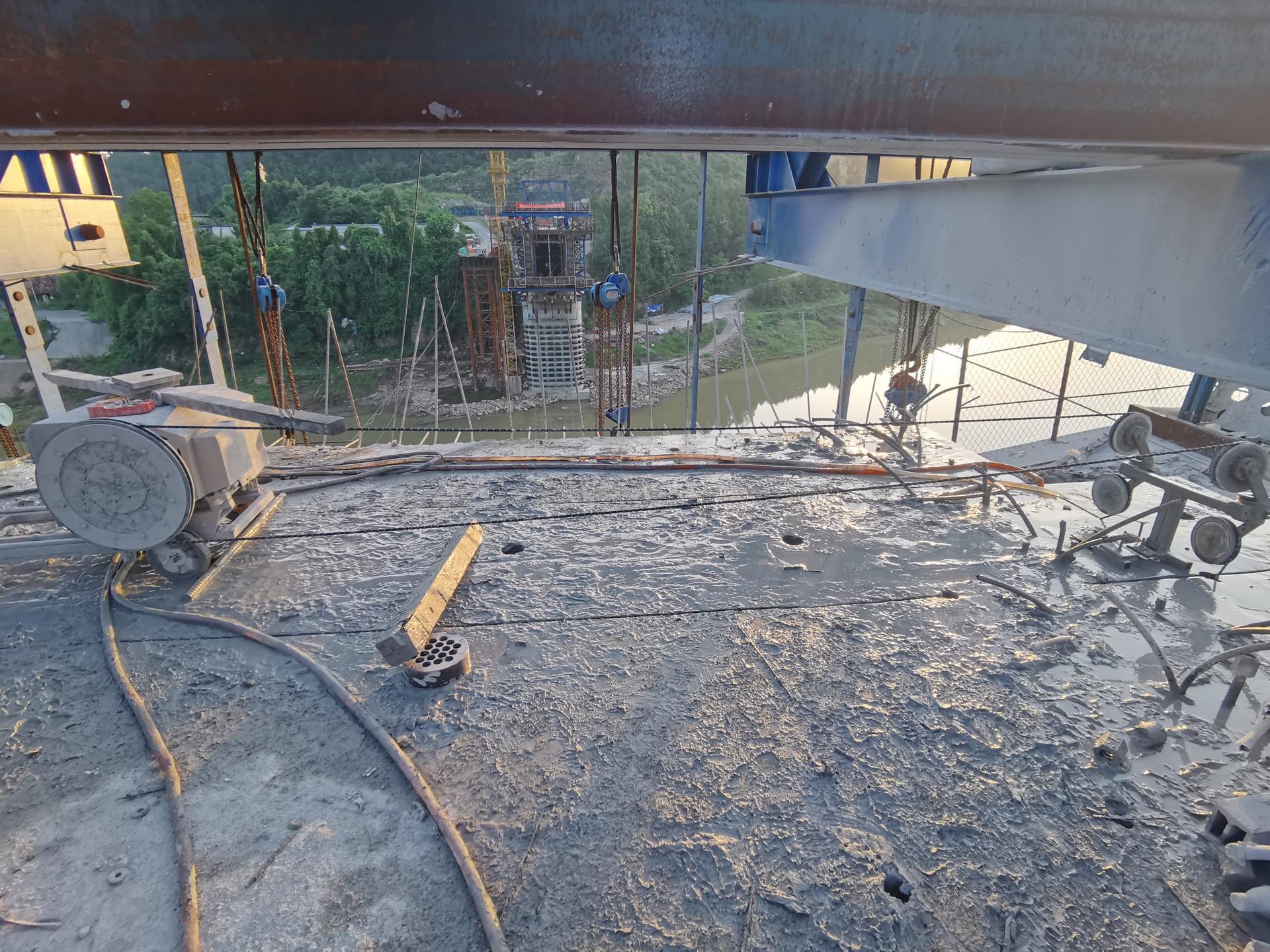 连续梁桥面绳锯切割全景：金刚石绳锯沿梁体纵横切割，河对岸桥墩支架施工同步进行