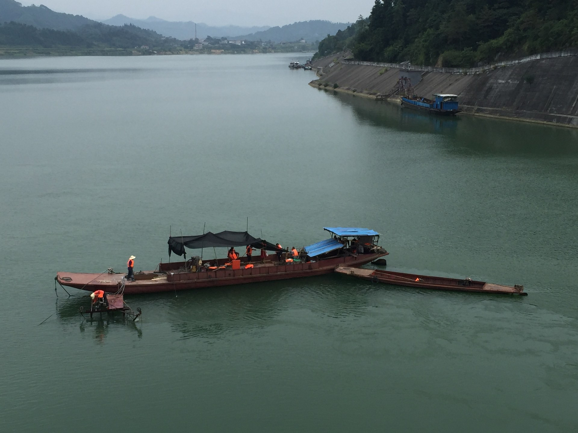 水下切割作业驳船全景：施工平台停泊在江心，临水混凝土护坡与山体在旁