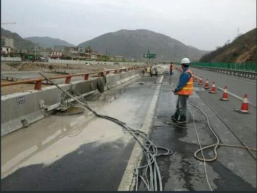高速防撞墙切割现场洒水降尘实拍：工人持水管冲洗切口，锥桶封闭作业车道